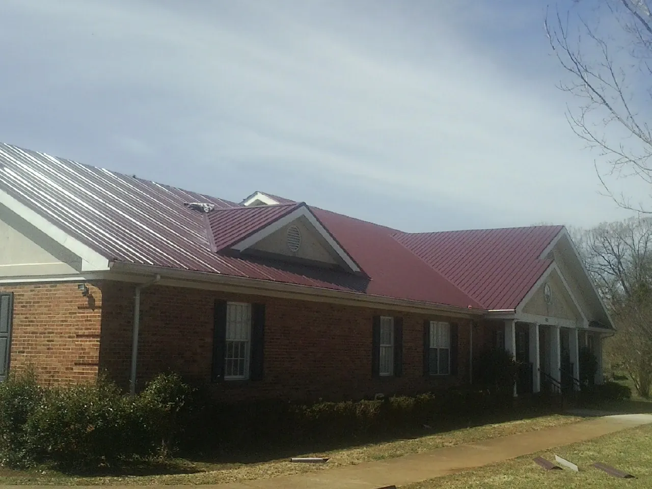Red metal roof with gabled entries on a long brick building, from a Hail Damage Roof Repair job in Burlingame