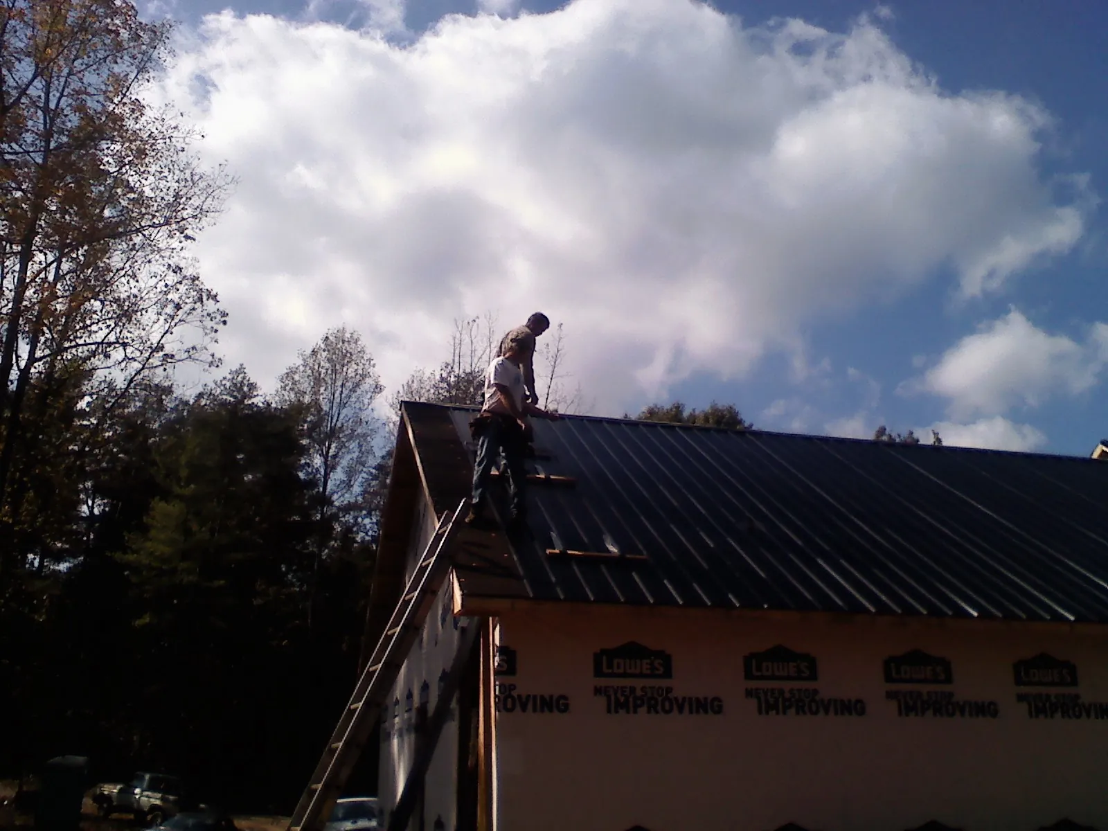 Roofer fastening dark metal panels high against a cloudy sky, from a Roof Inspection job in Burlingame