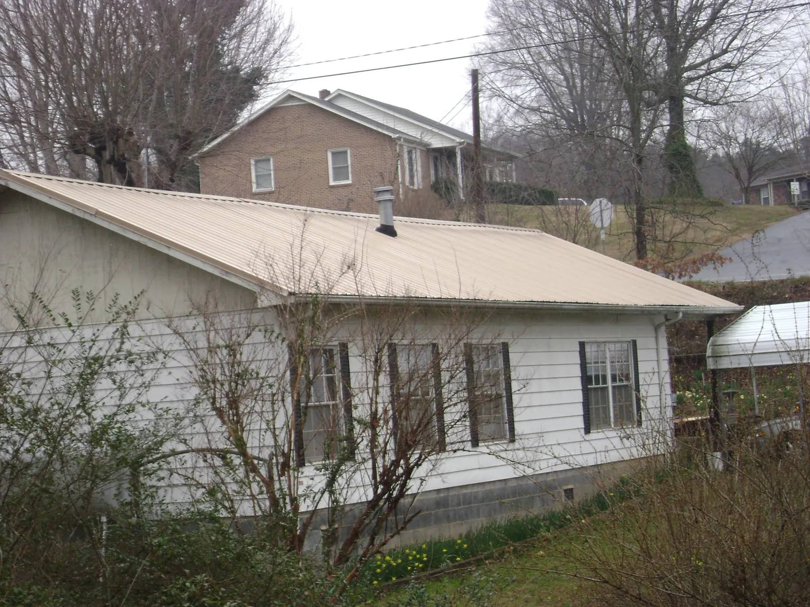 Tan metal roof on a white sided house set into a hillside — Commercial Roofing by Roofing Brothers in Burlingame